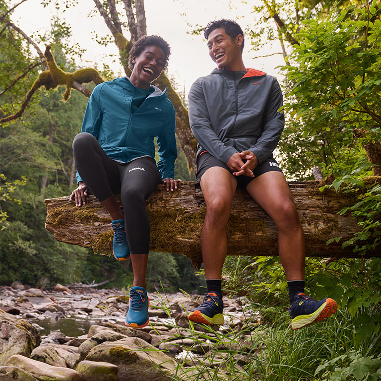 Pareja feliz con ropa HOKA sentada en un tronco
