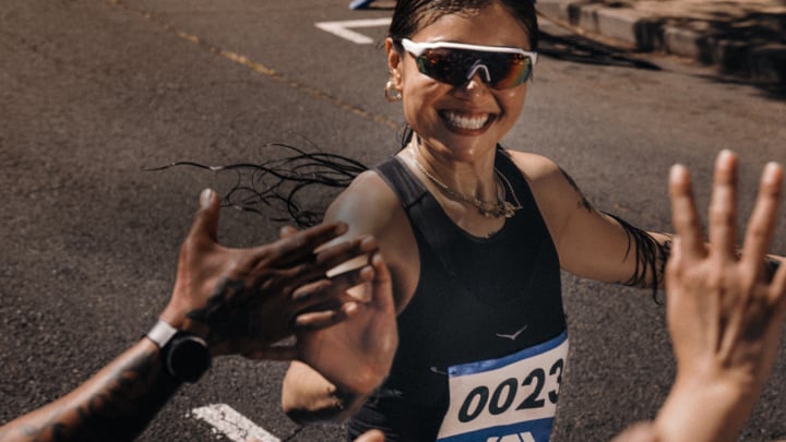 Coureur souriant portant des lunettes de soleil donnant des tapes dans les mains aux spectateurs pendant une course sur route ensoleillée.