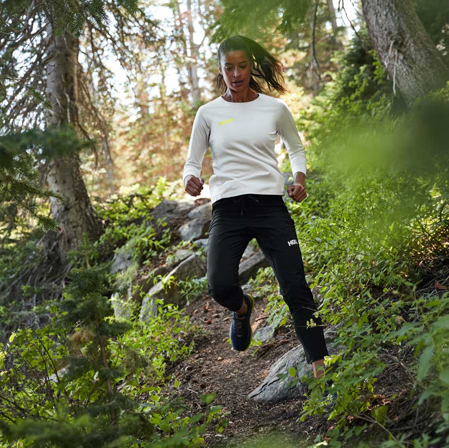 A woman running through the forest wearing HOKA shoes and apparel.