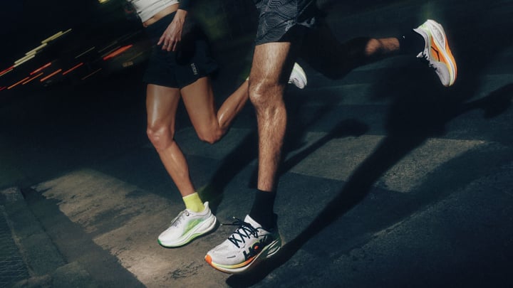 Gros plan de deux coureurs portant des chaussures de course HOKA et sprintant la nuit à travers une rue de la ville