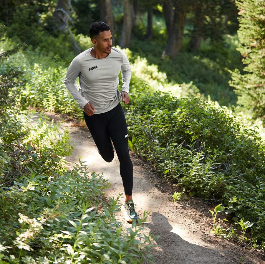 A man running through the forest wearing HOKA shoes and apparel.