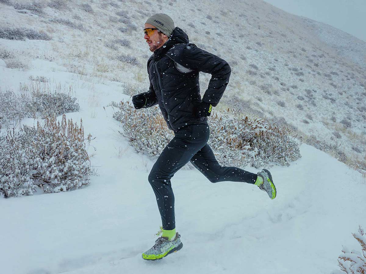 Personne courant sur une colline enneigée, avec des chaussures et de l’équipement HOKA.