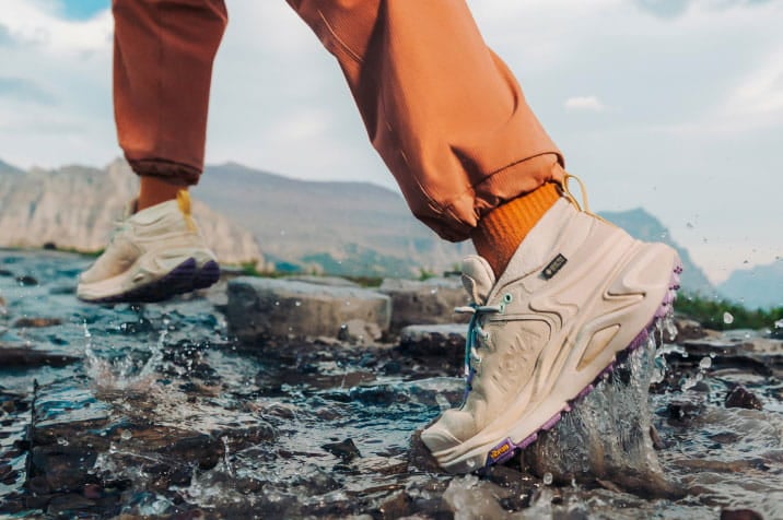Personne qui entre dans l’eau rocailleuse en chaussures HOKA.