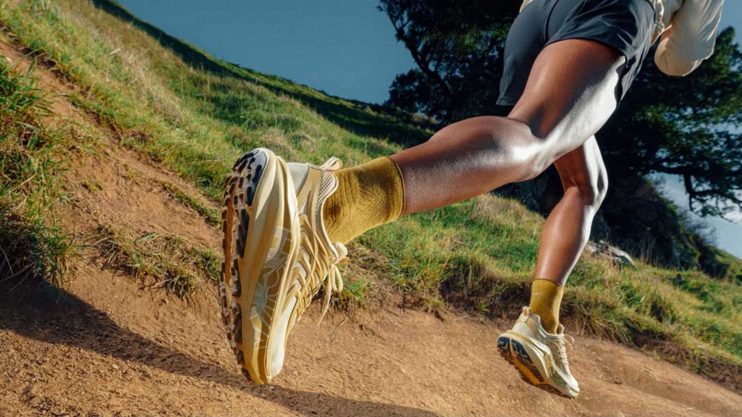 Vue en contre-plongée d’un athlète pratiquant la course sur sentier sur un chemin de terre avec des chaussures de couleur beige.