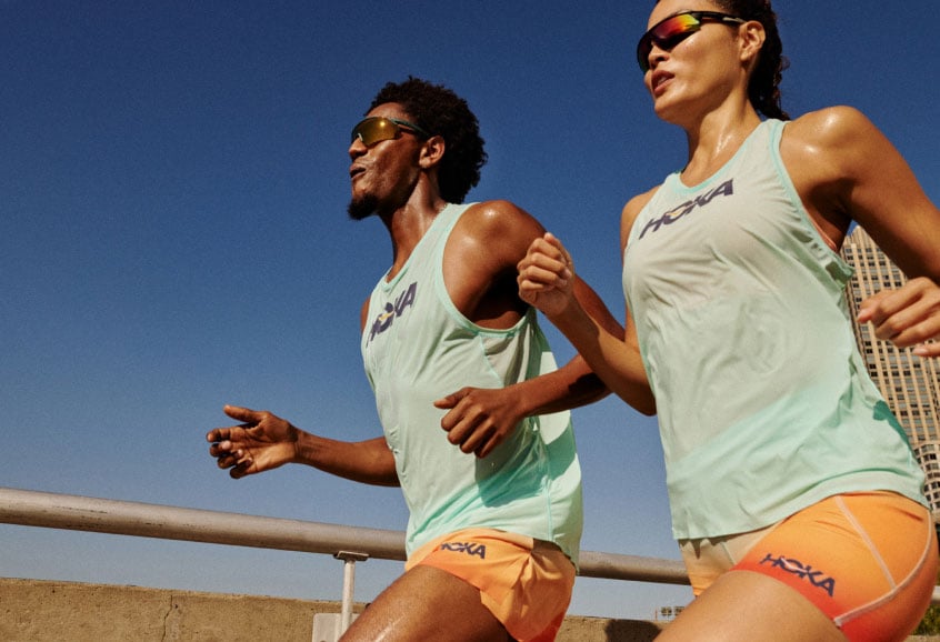 Two runners on an outdoor track, dressed in HOKA apparel.