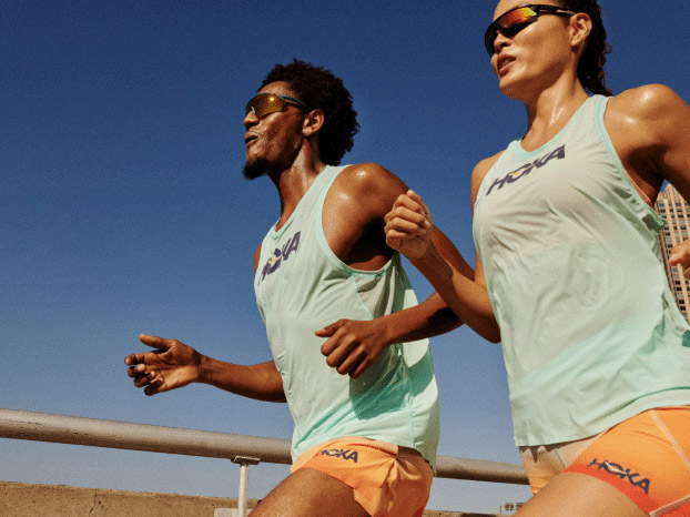 Two runners on an outdoor track, dressed in HOKA apparel.