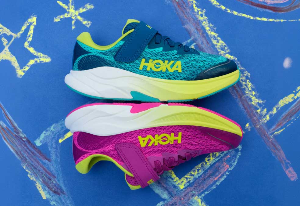Vue latérale des chaussures HOKA Little Kids en sélections colorées avec un papier bleu orné de traces de craie en arrière-plan.