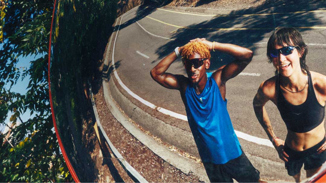 Reflet de deux coureurs en tenue de sport et lunettes de soleil posant sur une route extérieure.