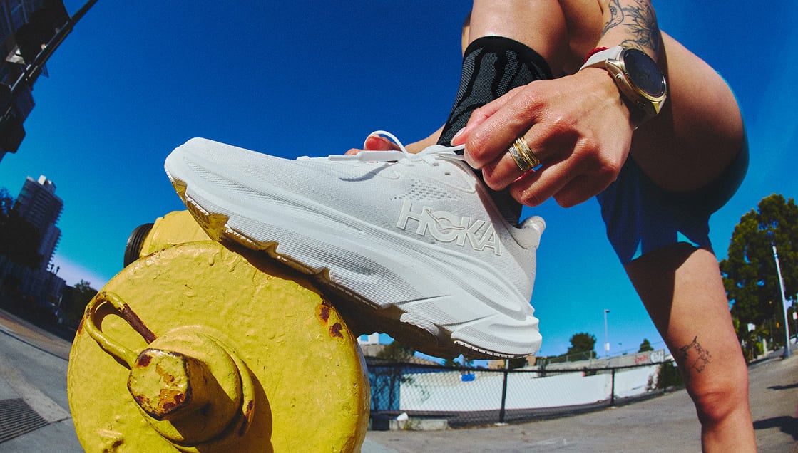 Un gros plan d’une personne en train de nouer les lacets de sa chaussure HOKA